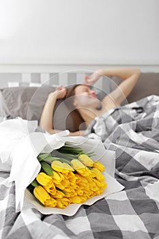 Happy Girl with flowers yellow tulips lying on a bed with enjoying flowers and romantic gift in Valentine day. She just woken up