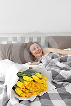 Happy Girl with flowers yellow tulips lying on a bed with enjoying flowers and romantic gift in Valentine day. She just woken up