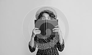 happy girl with frizz hair hiding behind book on yellow background