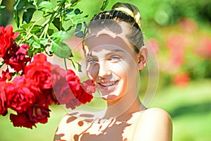 Happy girl in a garden with red roses. Beautiful young woman smelling a rose flower.