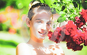 Happy girl in a garden with red roses. Beautiful young woman smelling a rose flower.