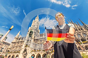 Happy girl with a German flag poses against the background of the city hall in Munich. Travel and immigration to Germany