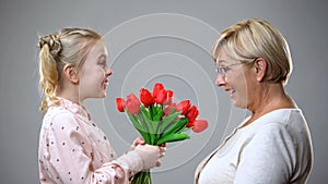 Happy girl giving flowers to grandmother, family tradition, holiday celebration