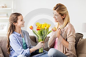 Happy girl giving flowers to mother at home