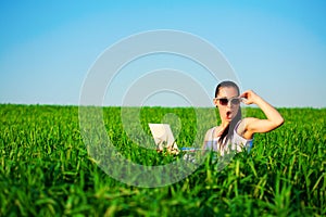 Happy girl in a green field with a laptop. summer