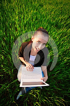 Happy girl in a green field with a laptop. summer