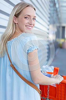 happy girl with groceries pushing cart on parking