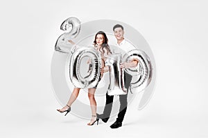 Happy girl and guy dressed in a stylish smart clothes are holding balloons in the shape of numbers 2019 on a white