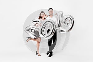 Happy girl and guy dressed in a stylish smart clothes are holding balloons in the shape of numbers 2019 on a white