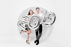 Happy girl and guy dressed in a stylish smart clothes are holding balloons in the shape of numbers 2019 on a white