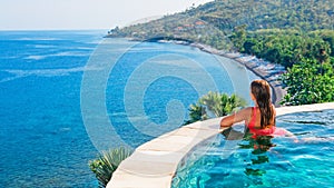 Woman at edge of infinity swimming pool with sea view