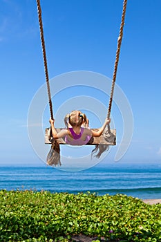 Happy girl have fun swinging high on sea beach
