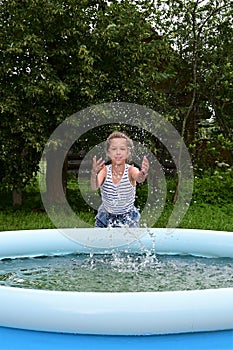 happy girl is having fun splashing water in inflatable pool in garden, refreshing herself in hot weather.