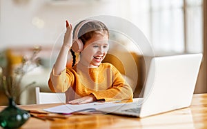 Happy girl in headphones raises her hand for a response during online lesson