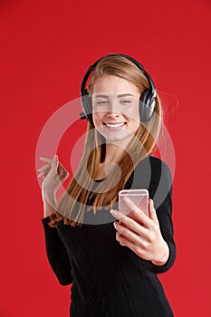 Happy girl with headphones, smiling and holding mobile phone on outstretched hand. On a red background.