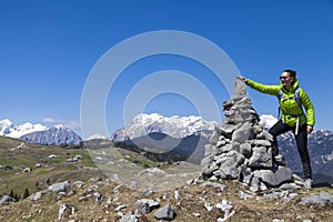 Happy girl hiker putting stones, small rocks on stone stack, high in mountains