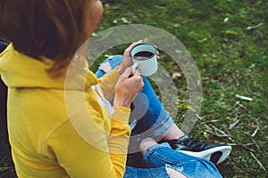 Happy girl holding in hands cup of hot tea on green grass in outdoors nature park top view, beautiful woman hipster enjoy drinking