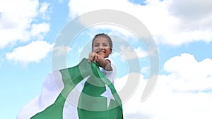 Happy girl holding Pakistan flag dancing outdoor under sunny sky.