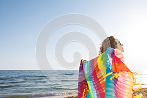 Happy girl holding rainbow fabric on the beach