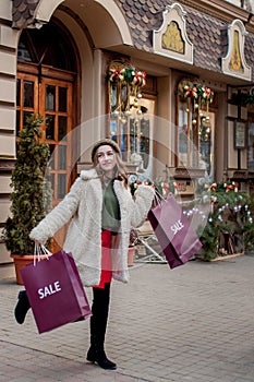 Happy girl holds paperbags with symbol of sale in the stores with sales at Christmas, around the city. Concept of shopping,