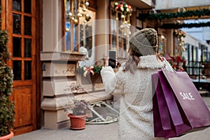 Happy girl holds paperbags with symbol of sale in the stores with sales at Christmas, around the city. Concept of shopping,