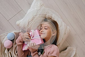 Happy girl hugging a Christmas gift box. Kid lying on a pillow and holding a present