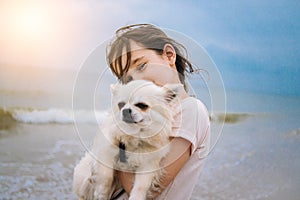 Happy girl hugging her little dog breed chihuahua at seashore against blue sky close up. Best friends rest and have fun