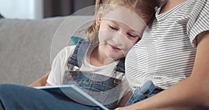 Happy girl hugging mother while reading book on grey couch