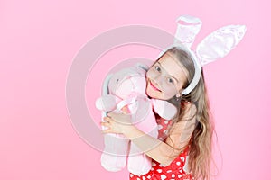 Happy girl hugging rabbit toy on pink background