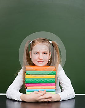 Happy girl hugs pile books near empty green chalkboard