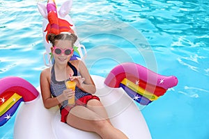 Happy girl with  on inflatable unicorn in swimming pool
