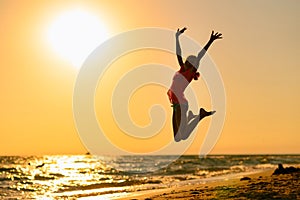 Happy girl jumping on the beach against the background of the sea and sunset.