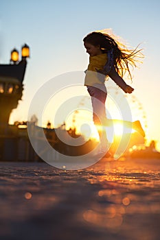 Happy girl jumping on the beach sand and enjoying the sunset in the fun city