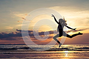 Happy girl jumping on the beach at the sunset time