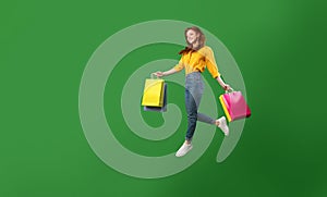 Happy Girl Jumping With Shopping Bags Over Green Studio Background