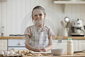 Happy girl kid in apron baking dessert in kitchen