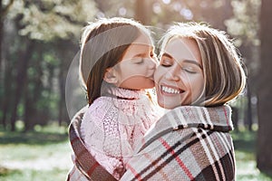 Happy, girl kisses her beautiful mother in forest are covered with blanket