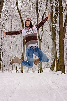 Happy girl in knitted cozy wear jumping in snowy winter forest. Christmas background. Attractive winter landscape. Jumping woman. photo