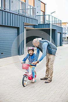 Happy girl laughing while her father teaching her to ride a bike