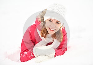 Happy girl laughs while lying on the snow in winter outdoors