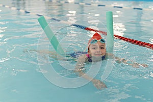 Happy girl learning to swim with pool noodle