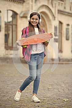 Happy girl listen to music in modern headphones holding skateboard urban outdoors, penny board