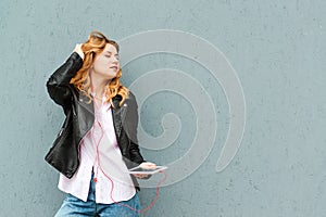 Happy girl listening to music outsite. Street style fashion, copy space. Pretty stylish student enjoying music with headphones.