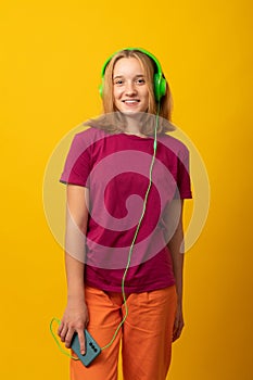 Happy girl listens music in headphones holds mobile phone chooses song from playlist dressed in casual t-shirt