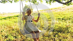 Happy girl with long hair swinging on swing on tree branch. On swing in the park happy girl. Slow motion. girl with long
