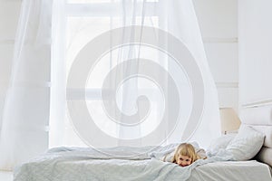 Happy girl lying down on bed in white room with window