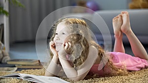 Happy girl lying on floor, reading book, developing imagination and creativity