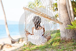 Happy girl lying in a hammock on the shore of a tropical beach.