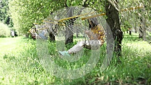 Happy girl lying on hammok and using smartphone outdoor. Woman with mobile phone sit in hammock in summer garden. Young female res