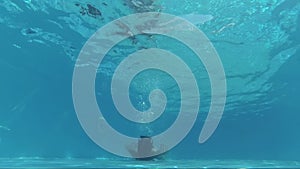 Happy girl in a mask under the water in the swimming pool lies down on the back, looks into the camera, bubbles